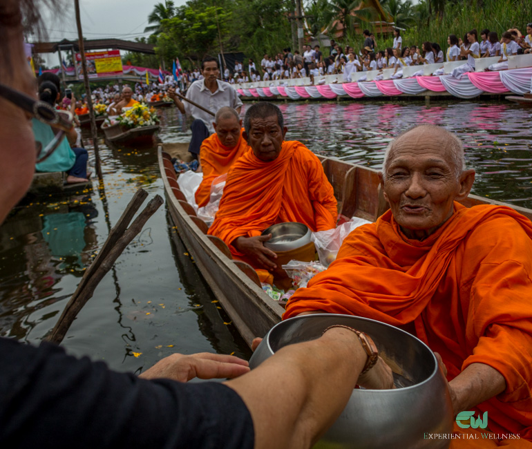 Thai people give alms to monks along a local canal