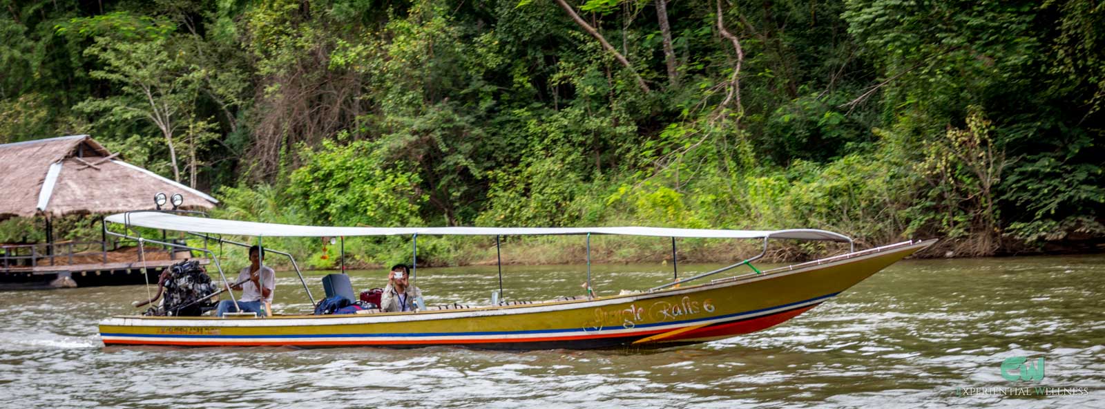 A long-tail boat is cruising through the river in Kanchanaburi