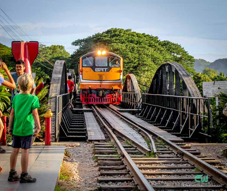 Young tourists and arriving train on the Bridge over the River Kwai