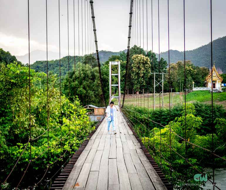 A girl is crossing a wooden hanging bridge back from a local Thai temple